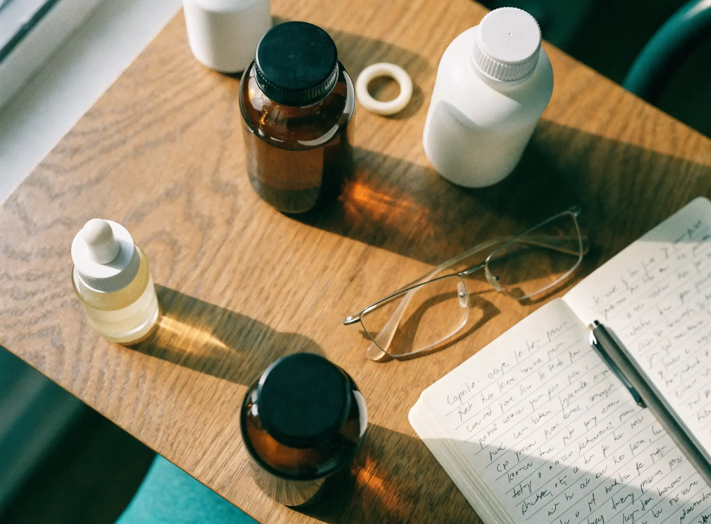 A desk with unlabelled supplement bottles, a dropper, a silicone ring and an open notebook of handwritten test notes