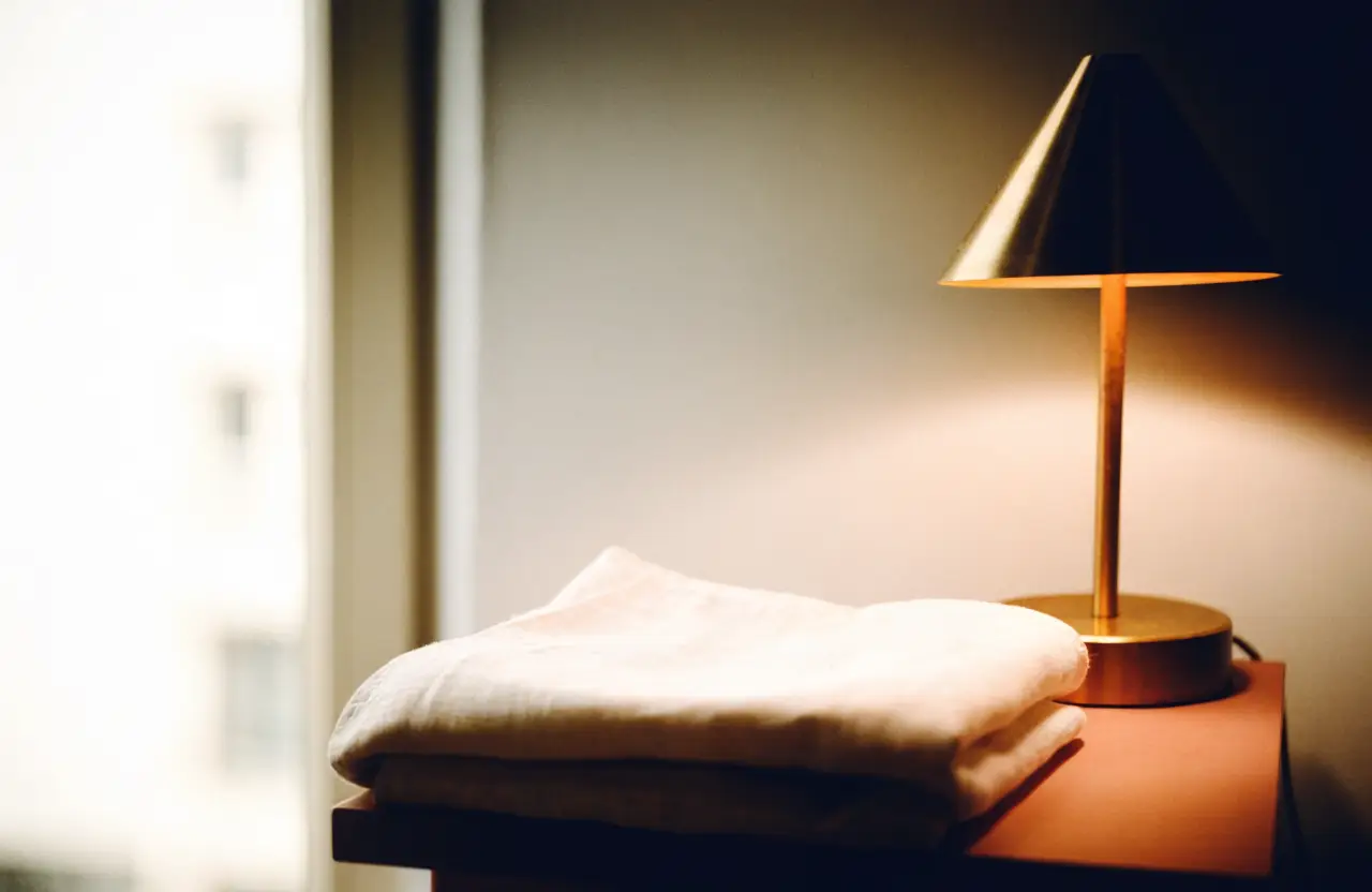 A folded linen sheet and a brass lamp on a bedside table