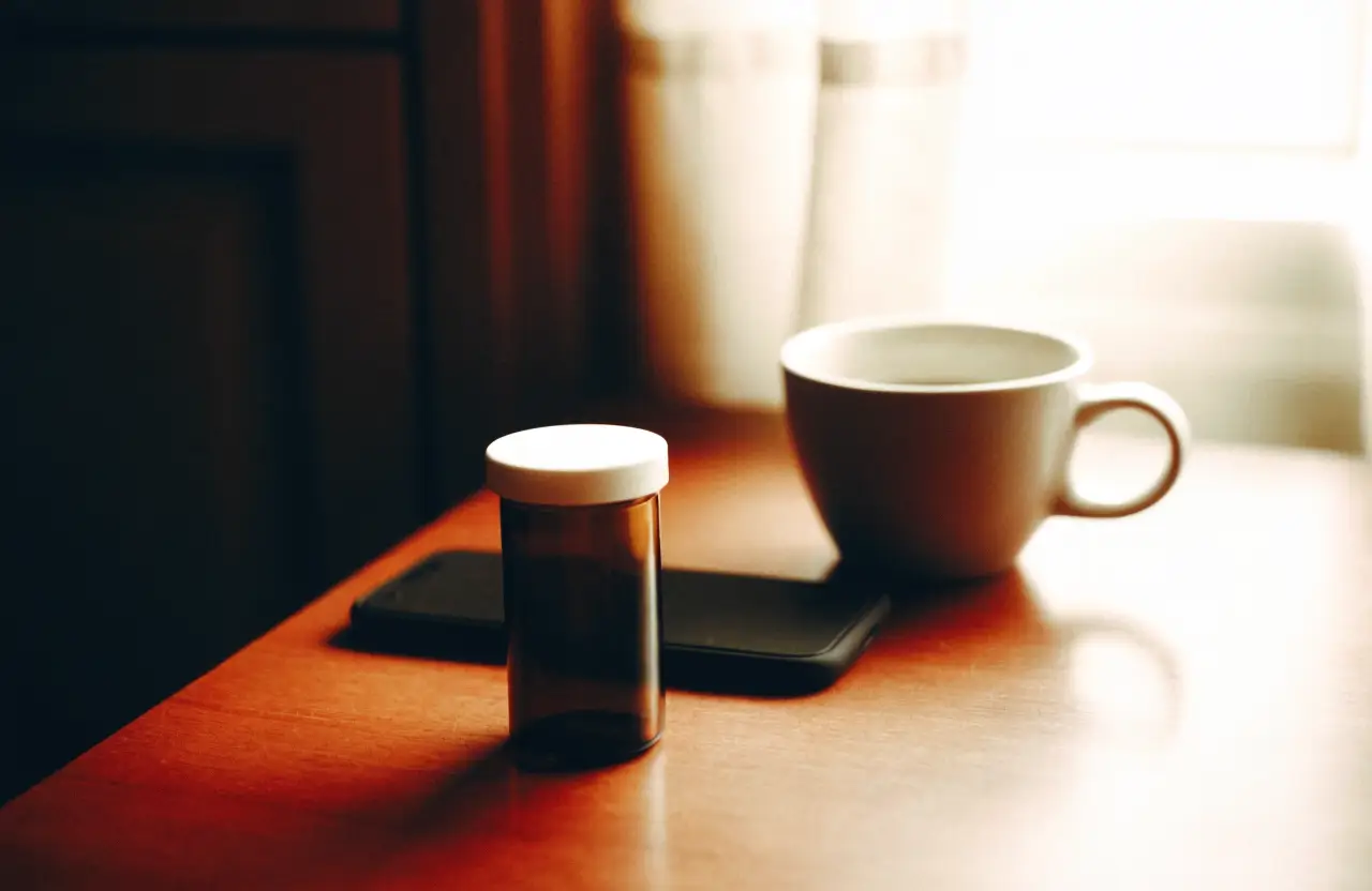 An amber pill bottle and a phone face down on a kitchen counter